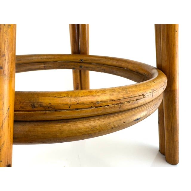A sculptural bentwood stool featuring a warm rattan frame with gracefully curved legs and a circular stretcher base. The...