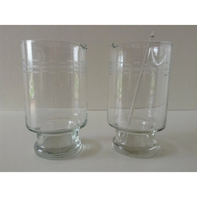 Vintage; Mid-Century era pair of etched glass Martini, footed cocktail mixers, with a single glass cocktail stirrer. In...