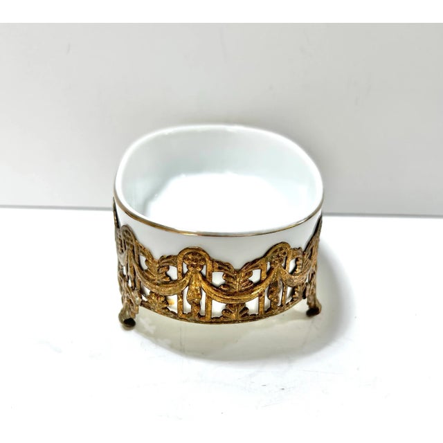 A 1970s Hollywood Regency soap dish featuring an ornate pierced gold-tone filigree surround with removable white porcelain...