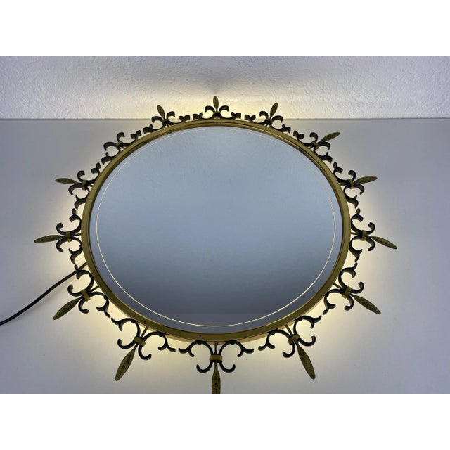 An illuminated round wall mirror from the 1960s made in Italy. The mirror has a circular brass design. The mirror is in a...