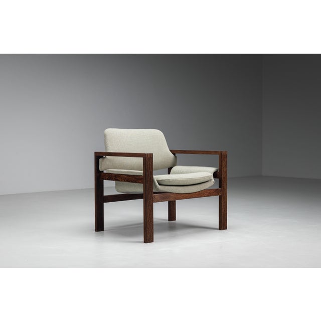 A striking mid-century lounge chair defined by its architectural cubic frame, crafted from solid wengé wood. The...