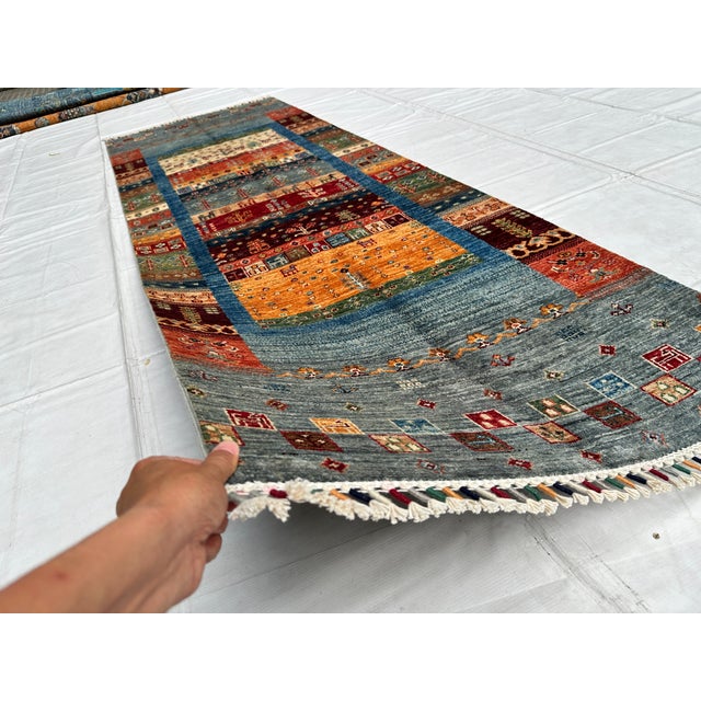 This hand-knotted Qashqai Gabbeh runner features horizontal bands of rust, gold, and indigo filled with small tribal...