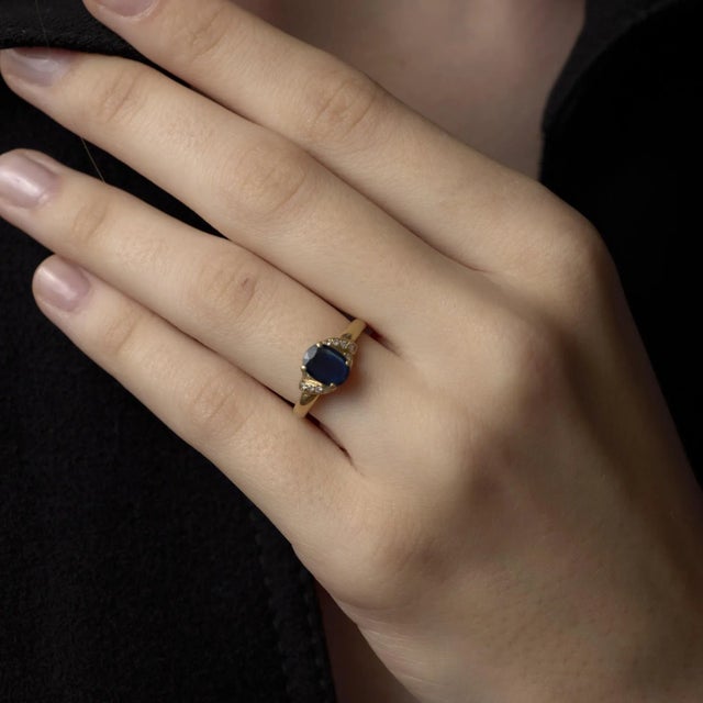 This vintage 14k yellow gold ring highlights a vivid cushion cut blue sapphire framed by sparkling diamond accents,...