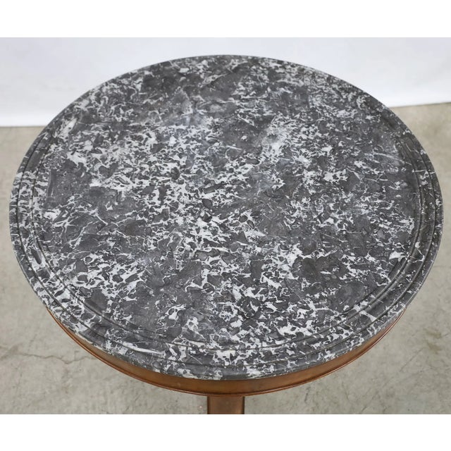 A striking 19th-century French Empire center table featuring a circular gray marble top with dramatic white veining and a...