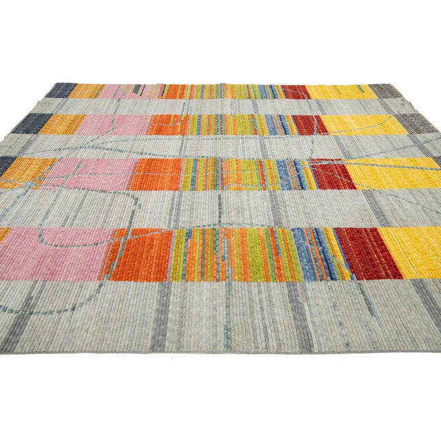 This hand-loomed modern wool rug boldly presents a stunning light gray background, accentuated by an intricate abstract...