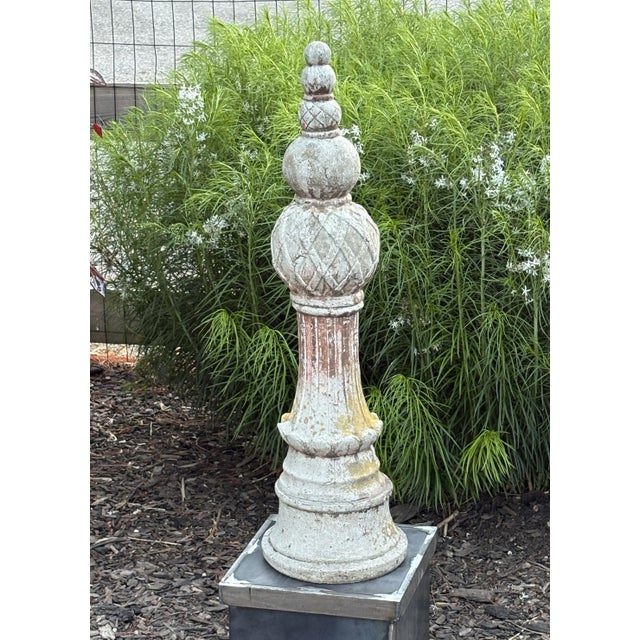 A tall, sculptural cast concrete finial with elegant tiered form and diamond-patterned detailing. The surface bears a...