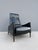 A sleek mid-century modern reclining lounge chair with black upholstered body, gently sloped high back, curved arms, and...