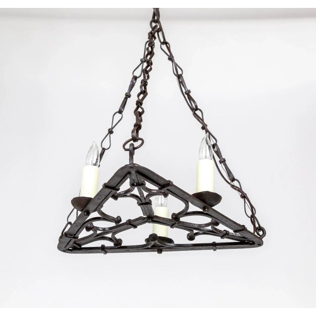 A Gothic style chandelier with three candle style lights on a flat, open, wrought iron base of curled, geometric shapes....
