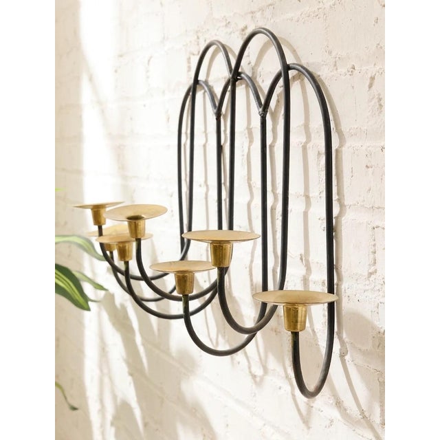 A wonderfully sculptural vintage wall-mounted candle holder combining looping black metalwork with warm brass candle cups....