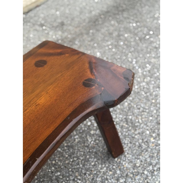 A rustic solid wood bench with an organically shaped live-edge seat, visible wood grain, and four slightly splayed legs....