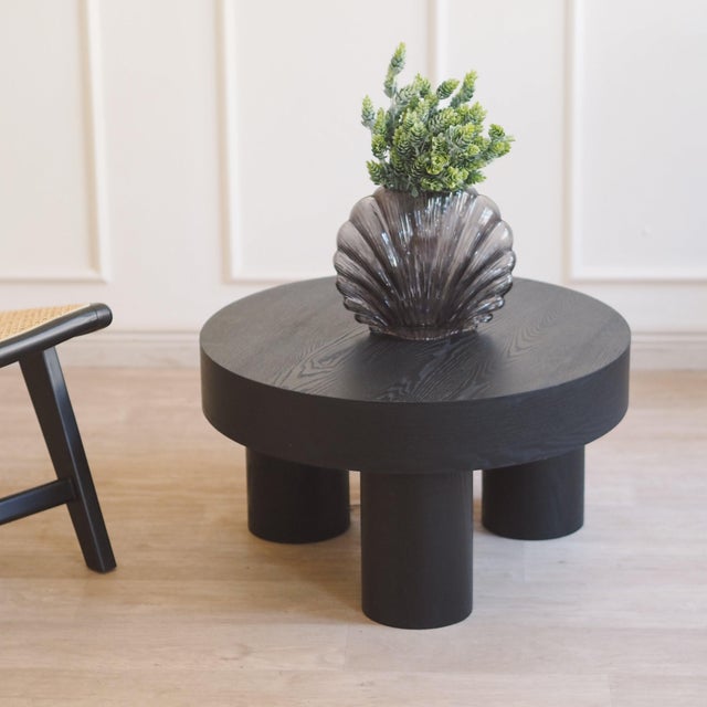The table is a newly produced piece of furniture with a round top and three cylindrical legs made of wood treated entirely...