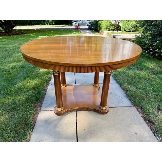 An Empire-style large round extension dining table by Baker Furniture with a glossy fruitwood top, reeded apron, four...
