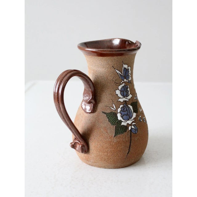 This is a vintage studio pottery pitcher. Signed by the artist, the handmade ewer features a hand-painted floral design...