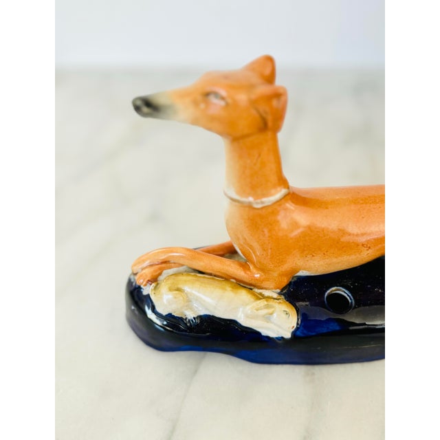 This exquisite Staffordshire (not marked) ceramic figurine showcases a graceful greyhound reclining beside a lifeless...