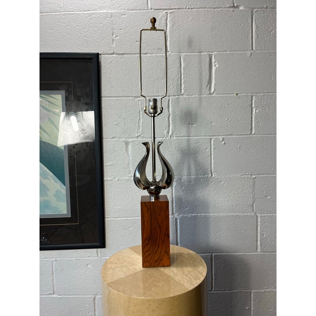 A sophisticated Mid-Century Modern table lamp featuring a highly polished chrome sculptural form rising from a solid...
