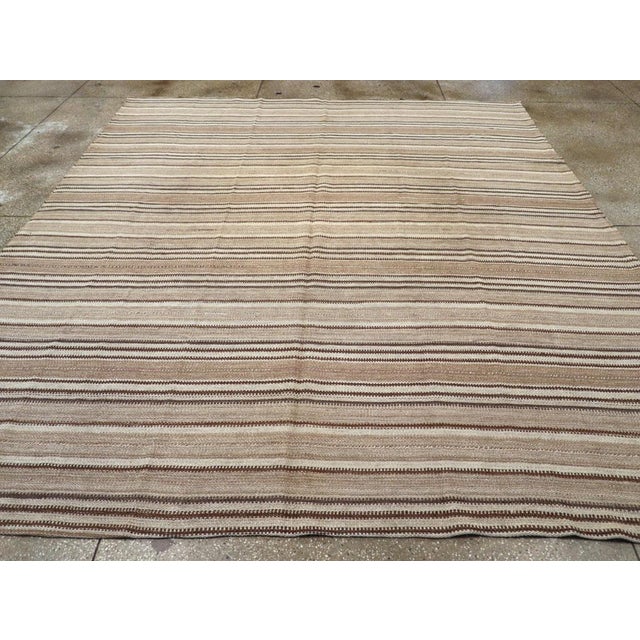 This Mid-20th century Turkish Flatweave Kilim rug, features a classic horizontal stripe design woven in soft, natural...