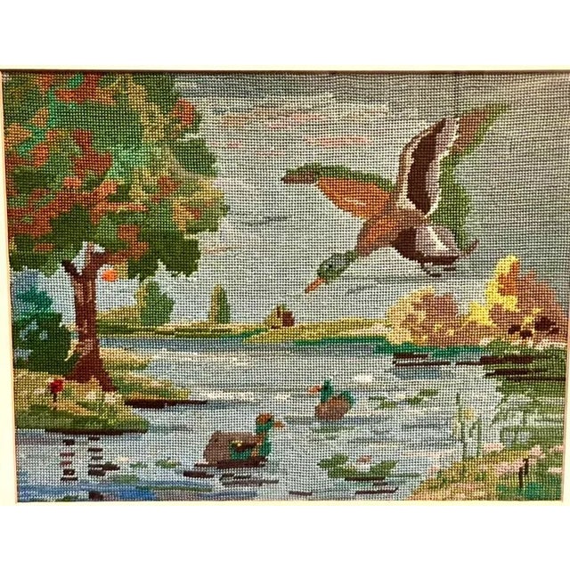 This vintage framed needlepoint artwork features a charming landscape scene of ducks on a river. It showcases lovely...