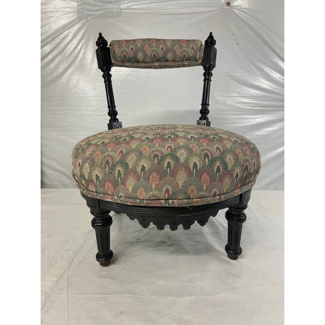 Single low round upholstered slipper or dressing chair with open back and black lacquered finish.