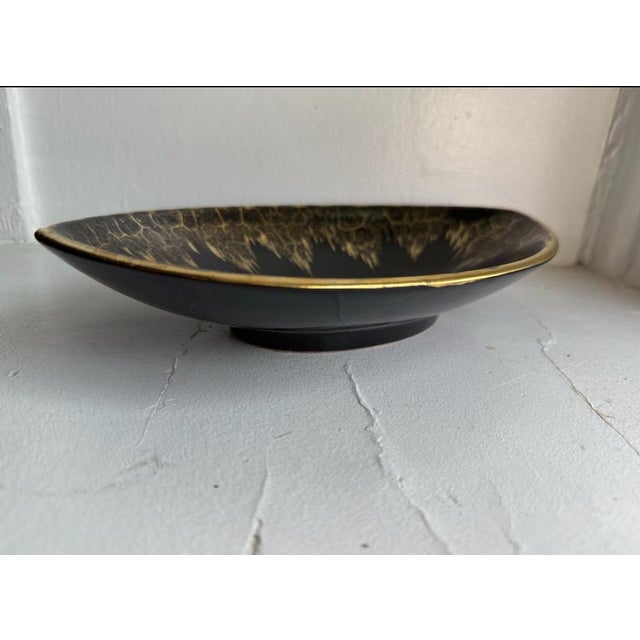 Mid-century ceramic bowl with a high-gloss black glaze and gold splash/crackle rim detailing. Shallow, open form designed...