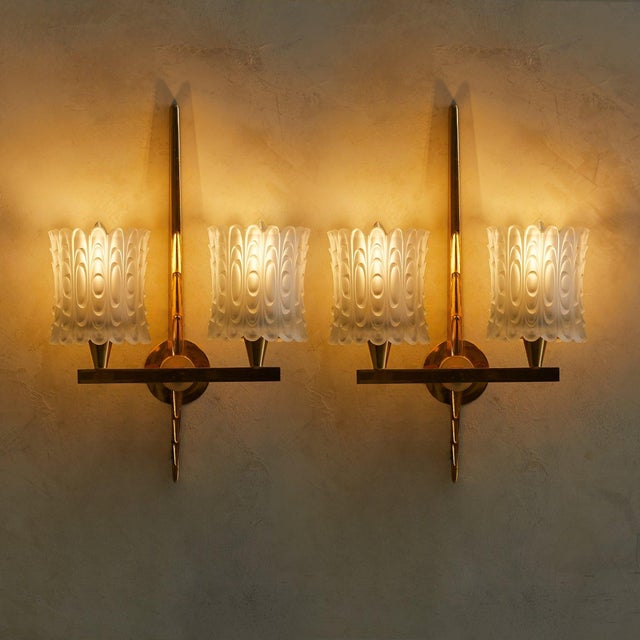 A pair of French sconces from the 1940s, attributed to Maison Arlus. A tapered brass stem rises vertically, its surface...