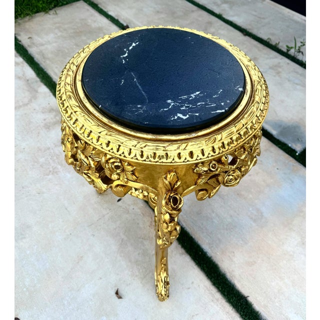 A beautifully ornate French-style side table featuring an elegant gold-leaf frame and a distinctive black marble top with...
