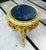 A beautifully ornate French-style side table featuring an elegant gold-leaf frame and a distinctive black marble top with...