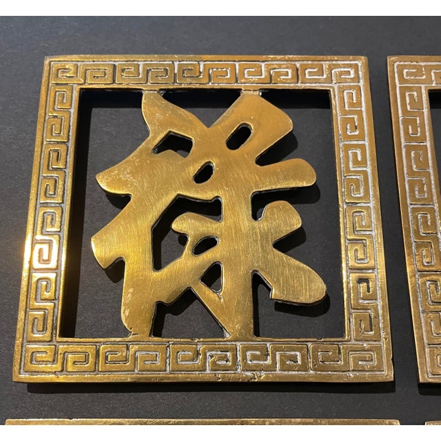 Set of four 4 x 4 inch brass trivets with Chinese characters and scrolling borders. Unmarked, each with a hanging loop.