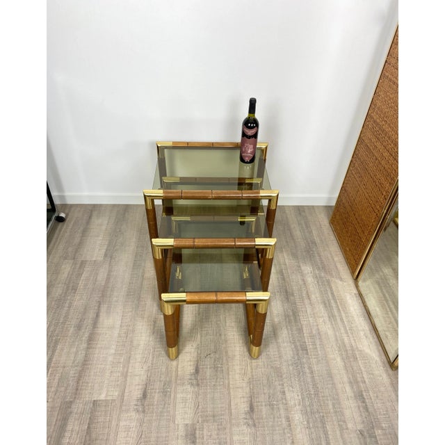 Three nesting tables featuring a wooden structure with brass corners and glass shelves in decreasing sizes. Dimensions:...