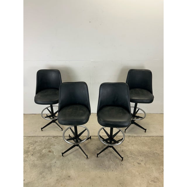 This set of four mid century modern bar stools feature original black vinyl upholstery, swivel seat atop a black painted...