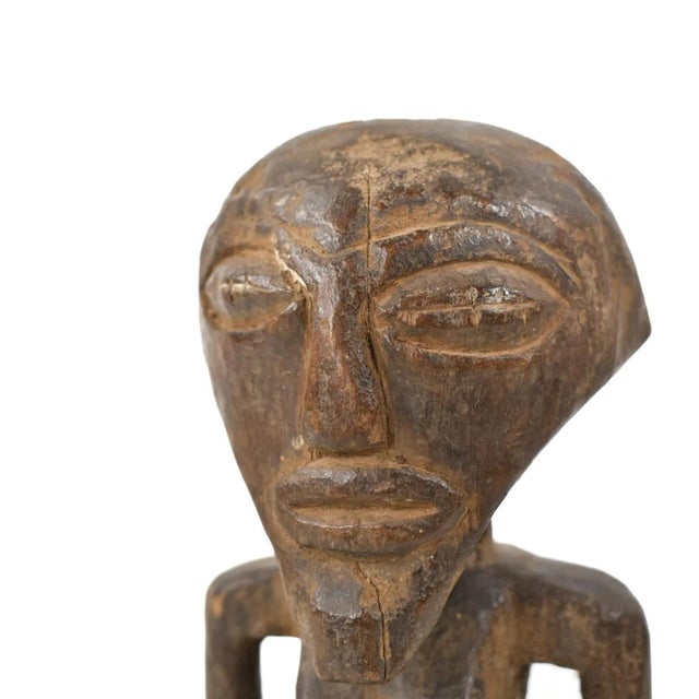 A standing Songye female miniature power figure, known as Nkishi, exhibits a cylindrical neck, shoulders rounded, and arms...