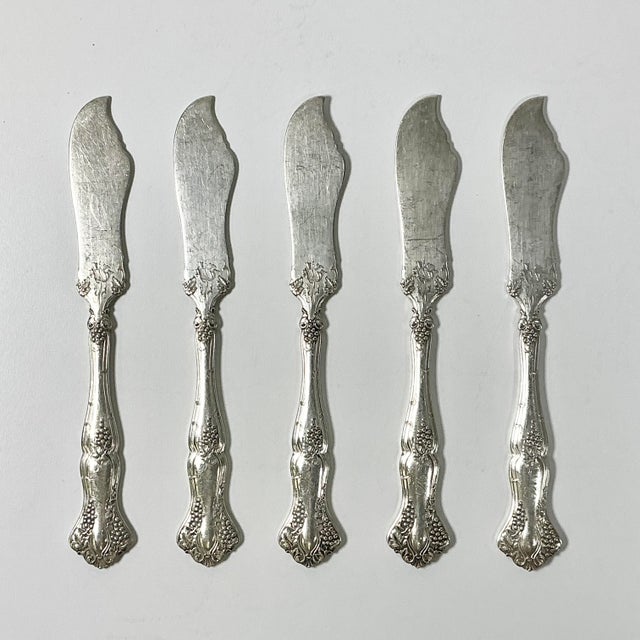 This set of six silverplated butter knives are from the 1930-40s era. They feature an ornate cut shaped blade and grape...