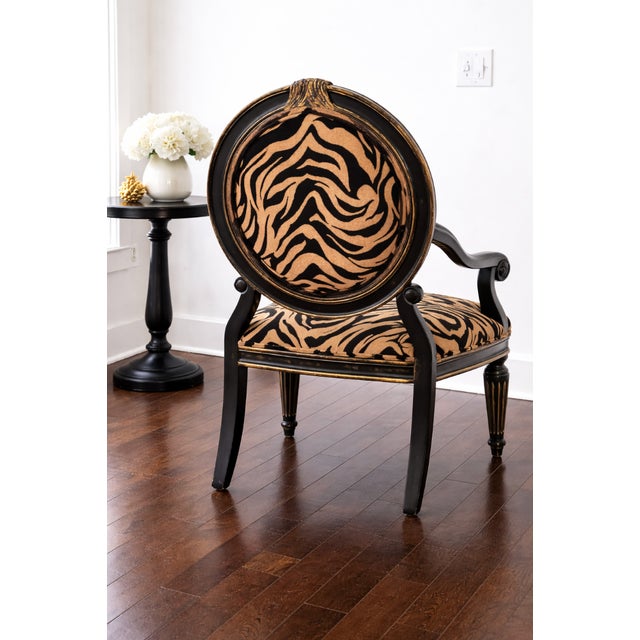 Striking Hollywood Regency–style armchair featuring bold zebra-pattern upholstery and a sculptural black wood frame with...