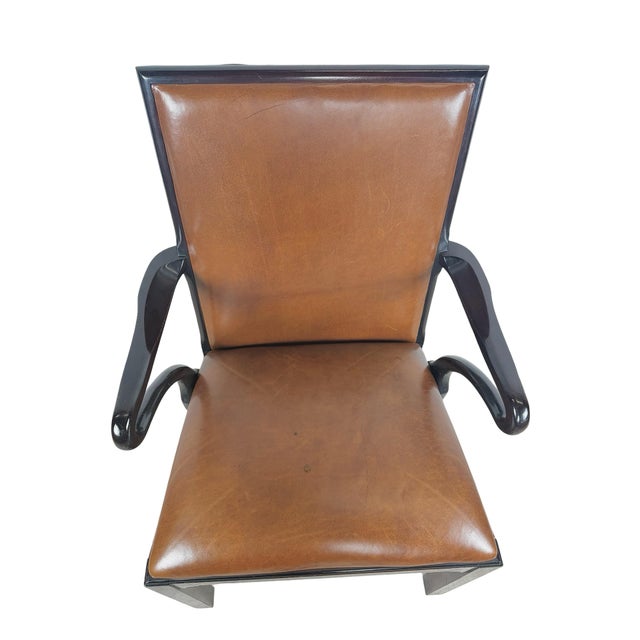 A sophisticated vintage armchair by Baker Furniture, pairing warm brown leather upholstery with an ebonized-finish wood...