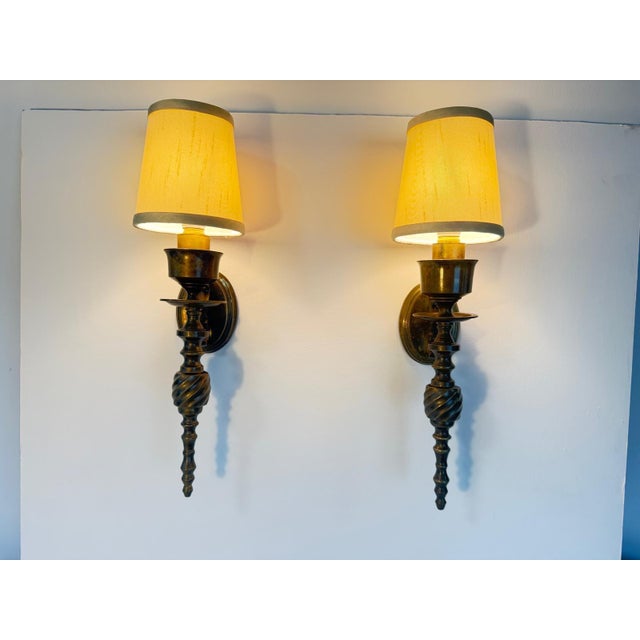 Pair of Wall Lights Sconces in brass, featuring an antique brass or bronze-toned metal body with a twisted-stem detail and...