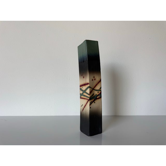 This striking 1990’s vintage studio pottery vase features a bold abstract design rendered in a tall, architectural...
