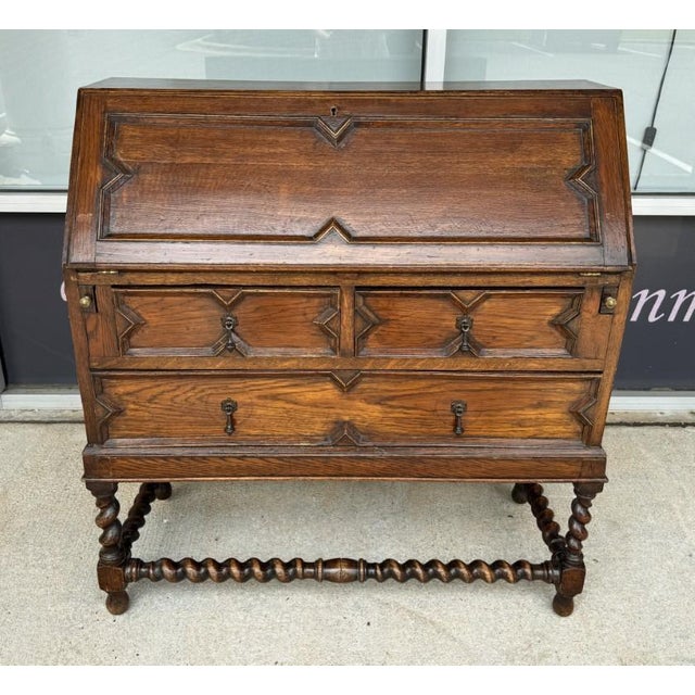 This circa 1900 oak secretary desk features a fall-front writing surface framed by bold geometric moldings and...