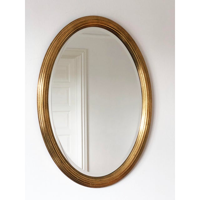 A beautiful vintage pair of gilded oval mirrors in gold from Deknudt mirrors Belgium. Carved wood and beveled glass....