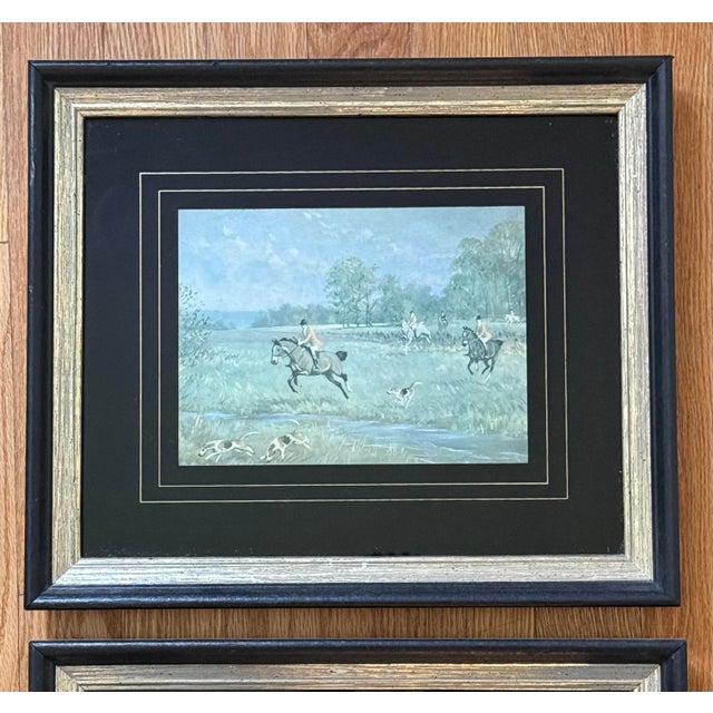 Midcentury pair of blue-toned equestrian fox hunt prints under glass, contrasted with a dramatic black mat and frame....