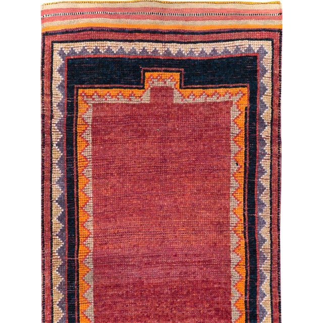 This mid-20th-century Turkish Anatolian runner presents a restrained composition centered on an open burgundy field. The...