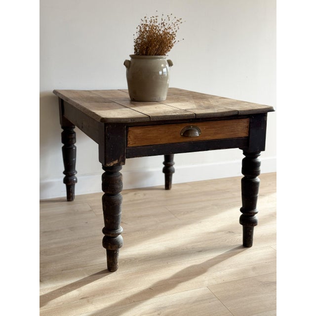 This antique English table features a single drawer with its original brass cup pull and a top of wide boards marked by a...
