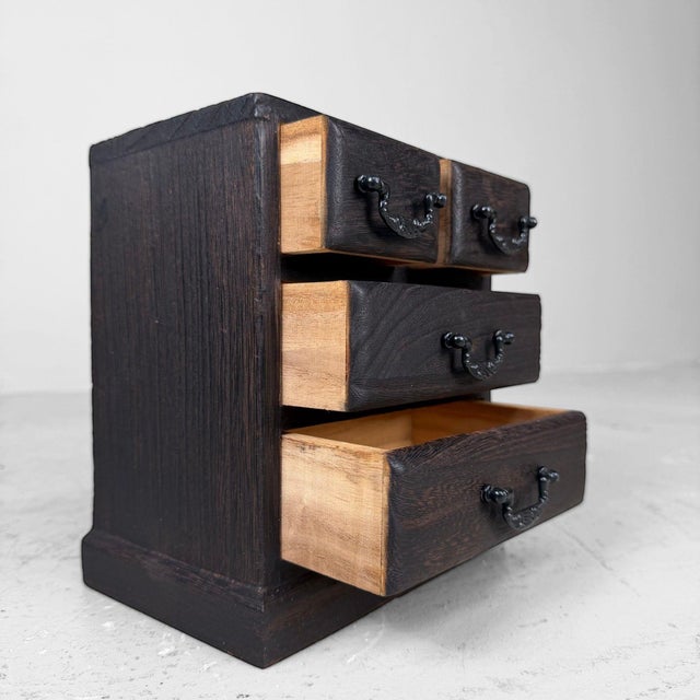 A compact Japanese drawer cabinet in traditional style, finished in dark wood with elegant black metal handles....