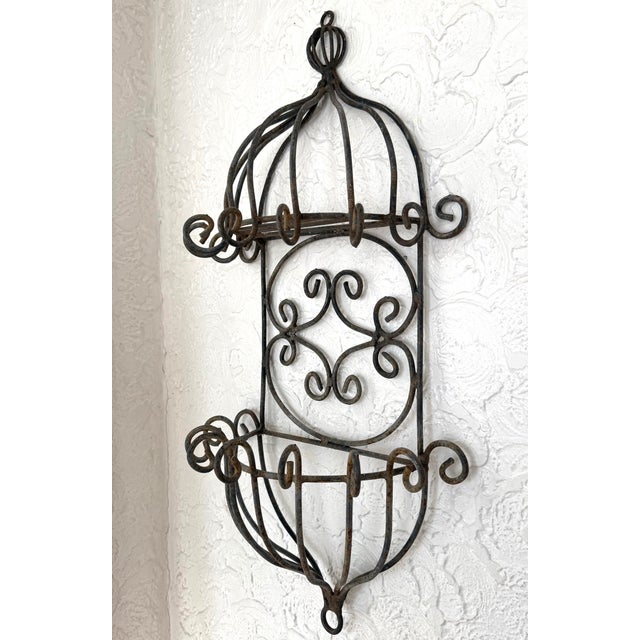 This is a vintage wrought iron wall planter with hanging rings at the top and bottom. The dark metal has a soft rust...
