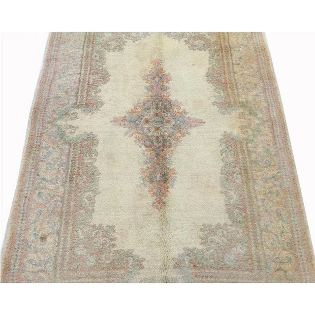 Old handwoven Kerman rug featuring a floral medallion on an ivory colored field and light blue border accented in shades...