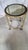 Round glass-top side table with a gold-tone metal frame, black border detail, and rolling casters. Measures 24″ tall × 20″...