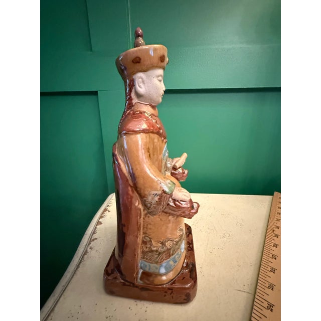 Vintage Chinese Emperor figurine in a sitting position. He is dressed in robes and wearing a hat. The rich colors of rust,...