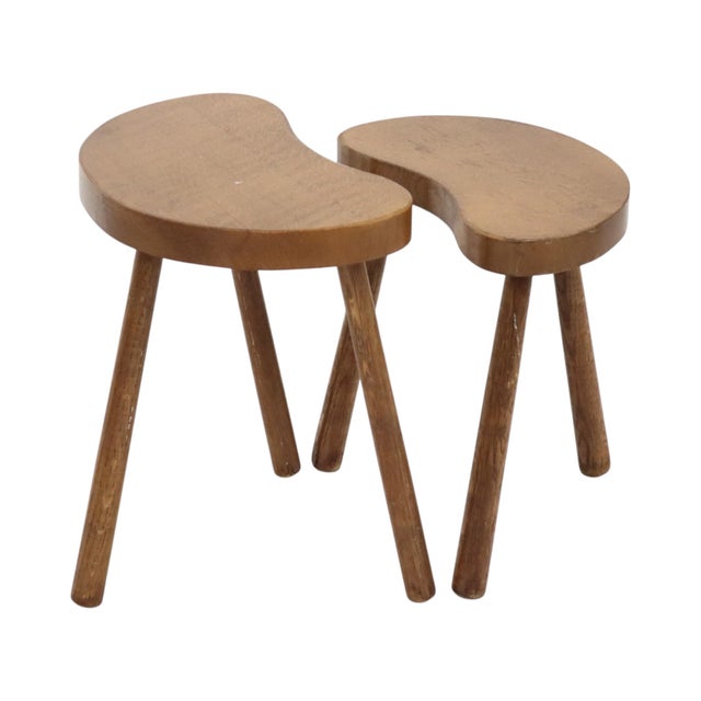 A nice set of two kidney-shaped, three-legged stools or nesting tables, crafted from solid wood (likely beech) and dating...