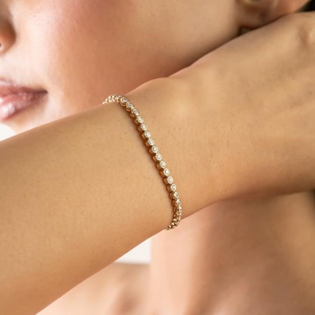 This elegant diamond tennis bracelet features round-cut natural diamonds totaling 1.37 carats, set in 18k yellow gold....