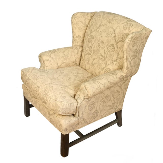 Upholstered English wingback chair in a neutral cream floral fabric and straight mahogany legs