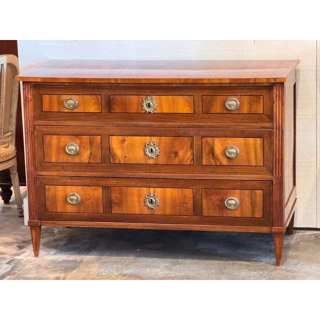 A three-drawer walnut commode with a banded inlay border on the top and a dark stringing line around each drawer front....