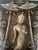 This intricately carved stone relief depicts a serene standing Buddha surrounded by attendants beneath ornate parasols, a...